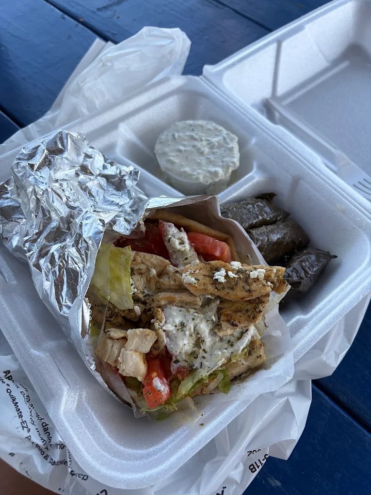 A chicken gyro in foil with three dolmades and a cup of tzatziki